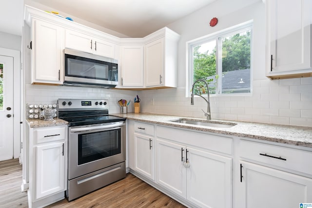 kitchen with stainless steel appliances, light wood-style flooring, decorative backsplash, white cabinets, and a sink