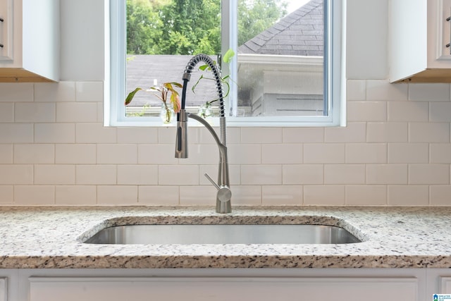 interior details with white cabinetry, a sink, and backsplash