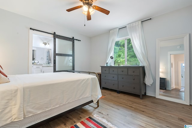 bedroom featuring a barn door, a ceiling fan, light wood-style flooring, and connected bathroom