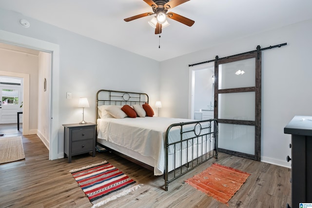 bedroom with a barn door, baseboards, ceiling fan, and wood finished floors