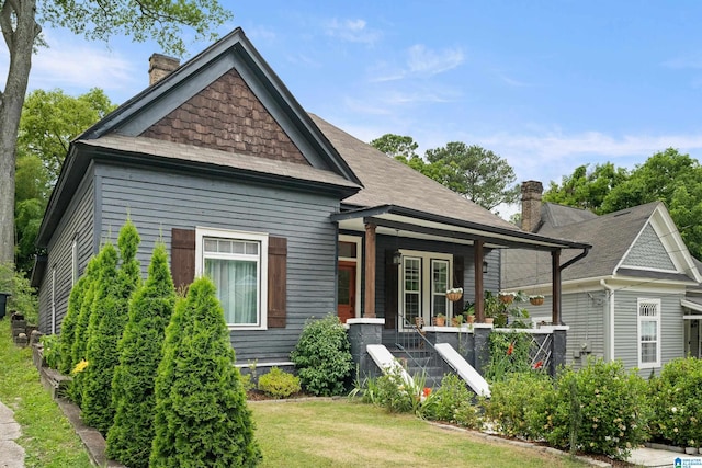 view of front of home with a porch, a front yard, and a chimney