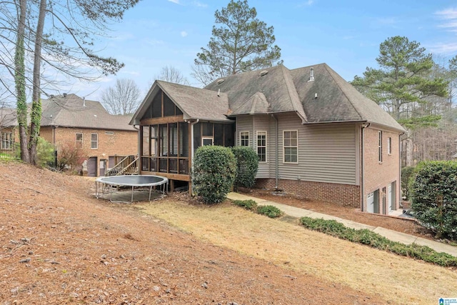 rear view of house with an attached garage, a sunroom, a trampoline, and roof with shingles