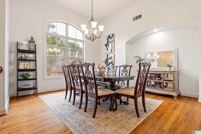 dining area with arched walkways, light wood-type flooring, visible vents, and a notable chandelier