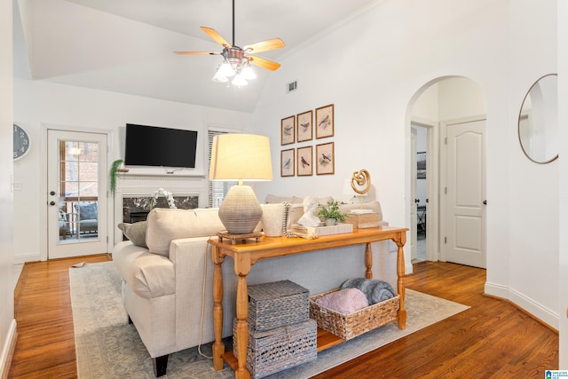 living area featuring arched walkways, a fireplace, wood finished floors, visible vents, and baseboards