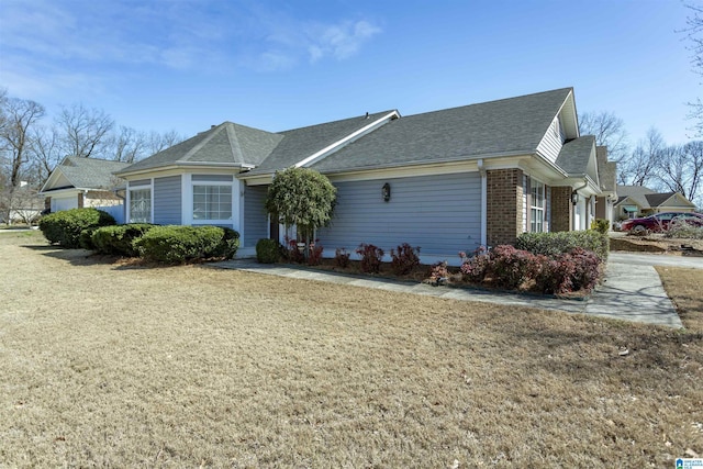 view of front of property featuring brick siding, a front lawn, and roof with shingles