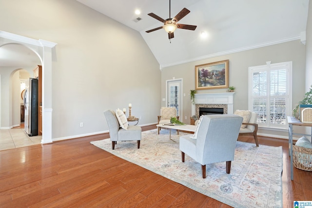 living area featuring light wood finished floors, visible vents, arched walkways, a fireplace, and high vaulted ceiling