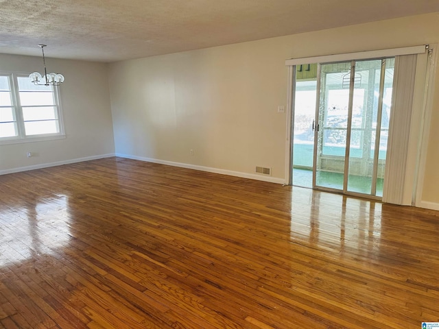 unfurnished room with a healthy amount of sunlight, visible vents, dark wood finished floors, and an inviting chandelier