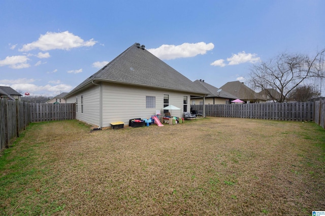 rear view of property with a fenced backyard, a shingled roof, and a lawn