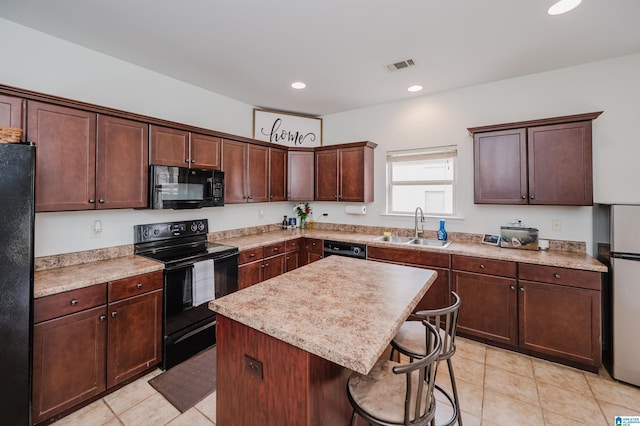 kitchen with visible vents, a kitchen island, a breakfast bar area, black appliances, and a sink