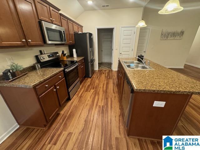 kitchen with dark wood-style flooring, decorative light fixtures, appliances with stainless steel finishes, a kitchen island with sink, and a sink