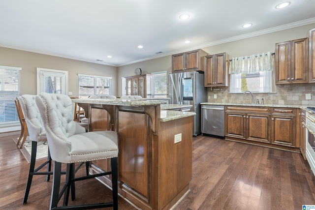 kitchen featuring light stone counters, stainless steel appliances, a center island, brown cabinetry, and a kitchen bar