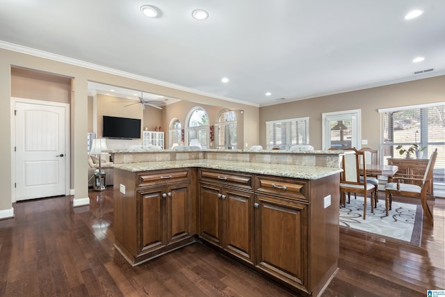 kitchen with dark wood-type flooring, a kitchen island, light stone countertops, and crown molding