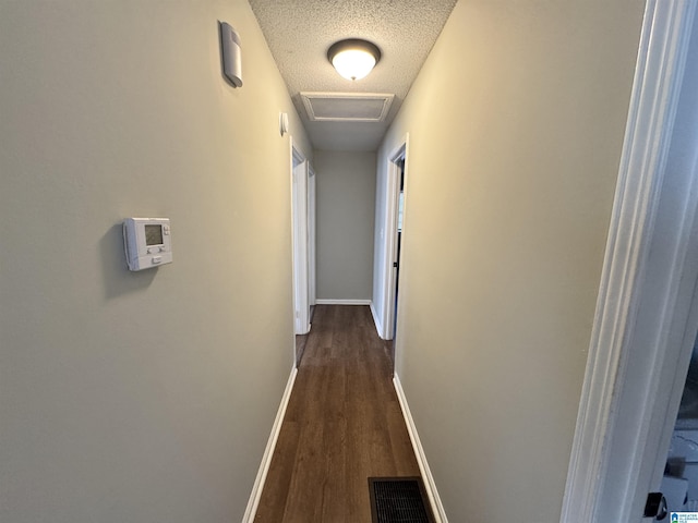 corridor featuring dark wood finished floors, visible vents, attic access, a textured ceiling, and baseboards