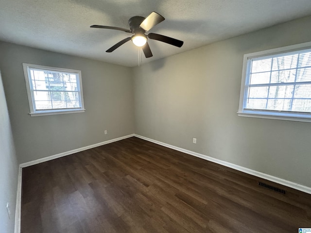 unfurnished room with a wealth of natural light, visible vents, dark wood finished floors, and baseboards