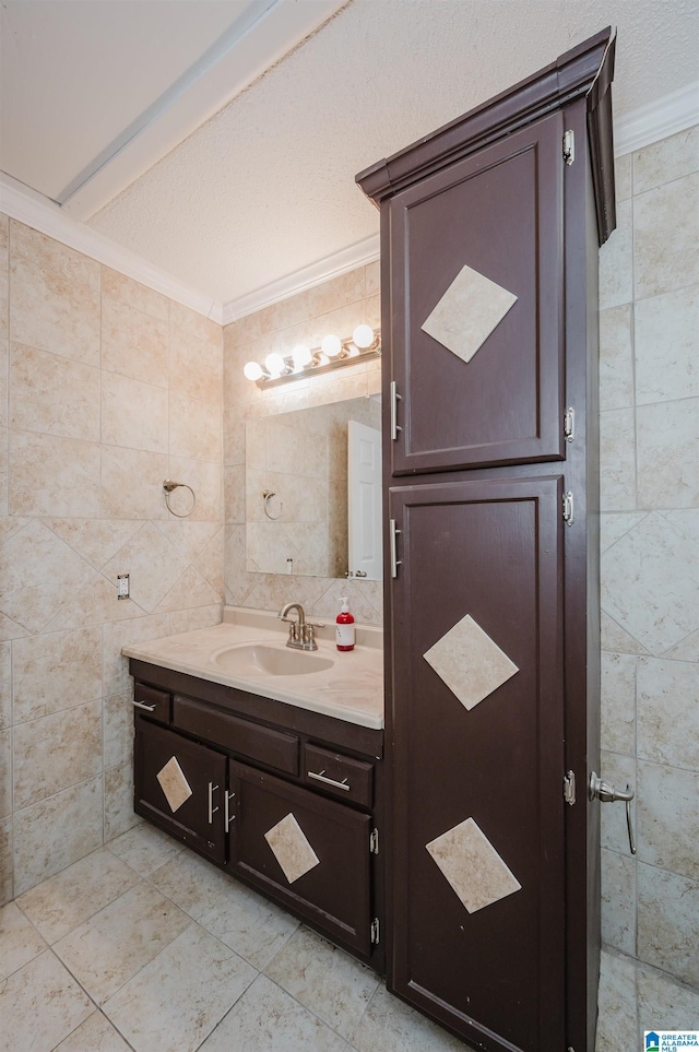 bathroom with a textured ceiling, ornamental molding, vanity, and tile walls