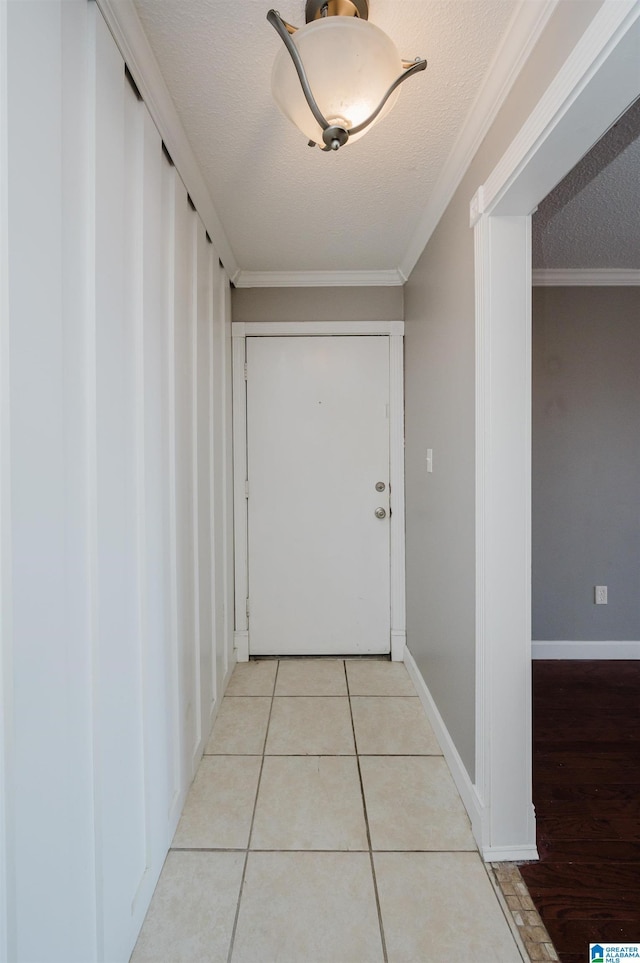 hallway with light tile patterned floors, a textured ceiling, baseboards, and crown molding