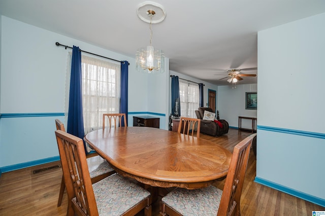 dining space featuring ceiling fan with notable chandelier, wood finished floors, visible vents, and baseboards