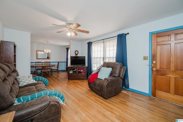 living room featuring ceiling fan with notable chandelier, wood finished floors, visible vents, and baseboards