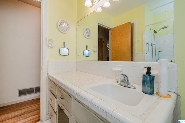 full bath with a shower, visible vents, backsplash, vanity, and wood finished floors