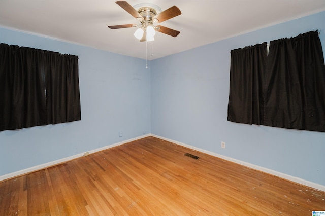 empty room with a ceiling fan, wood finished floors, visible vents, and baseboards