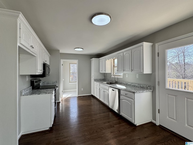 kitchen featuring appliances with stainless steel finishes, dark wood-type flooring, white cabinetry, a sink, and baseboards