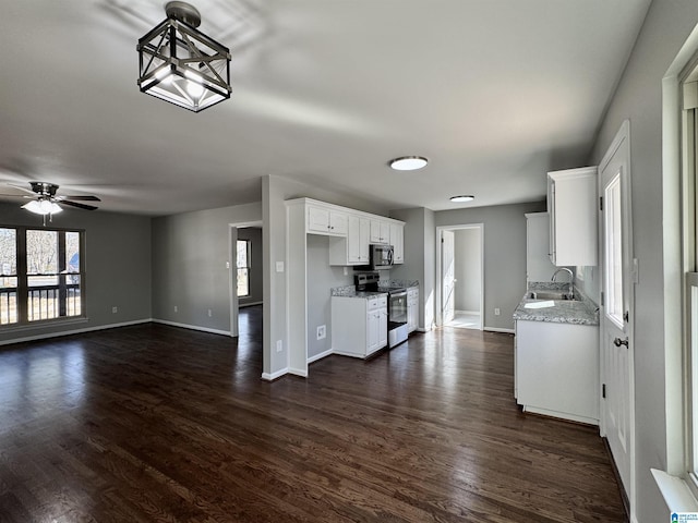 kitchen featuring stainless steel appliances, a sink, white cabinetry, open floor plan, and light stone countertops