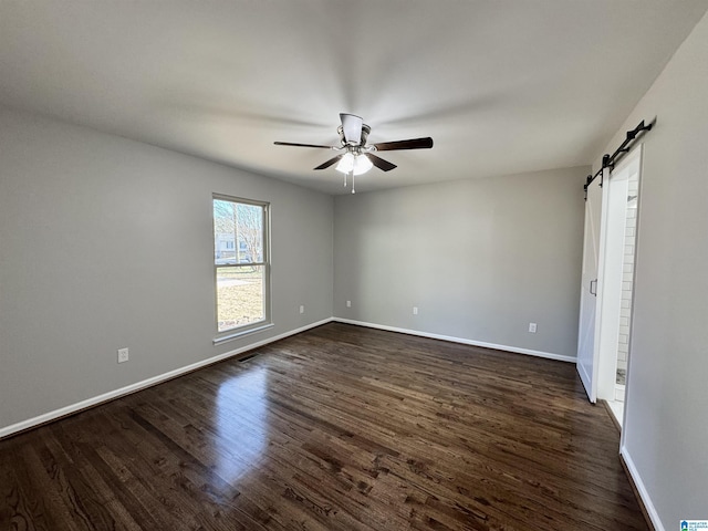 unfurnished bedroom with a barn door, visible vents, baseboards, a ceiling fan, and dark wood-style floors