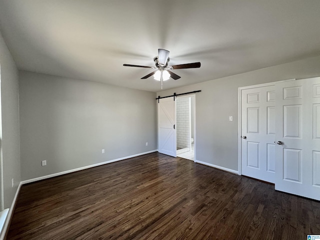 unfurnished bedroom with a ceiling fan, a barn door, baseboards, and dark wood-type flooring