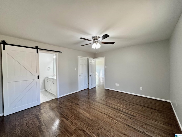 unfurnished bedroom featuring light wood finished floors, a barn door, ceiling fan, ensuite bath, and baseboards