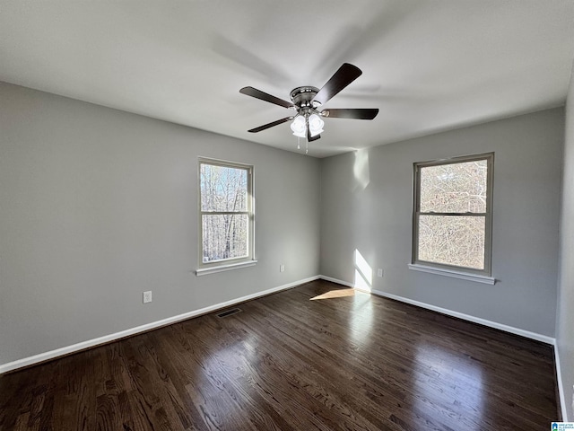 spare room featuring ceiling fan, baseboards, visible vents, and dark wood finished floors