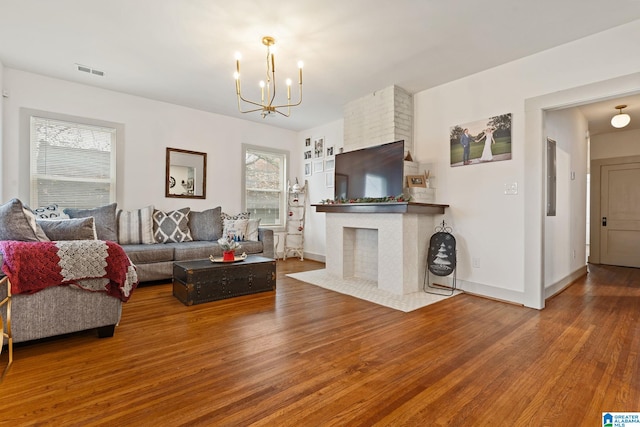 living area with baseboards, visible vents, wood finished floors, a fireplace, and a chandelier