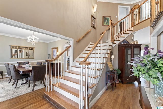 stairway featuring baseboards, a towering ceiling, ornamental molding, wood finished floors, and an inviting chandelier