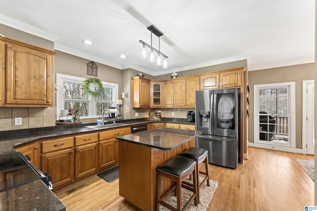 kitchen with a center island, decorative light fixtures, glass insert cabinets, a sink, and stainless steel fridge