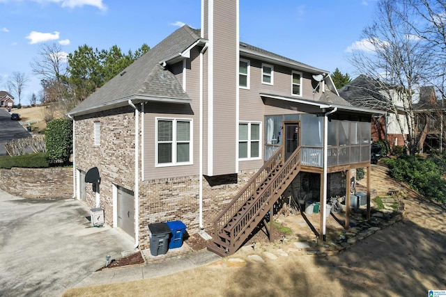 rear view of house featuring a sunroom, a chimney, an attached garage, stairs, and brick siding