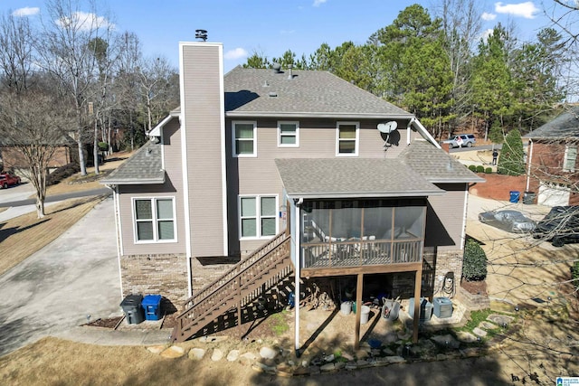 rear view of house with a chimney, a shingled roof, stairway, a sunroom, and central AC