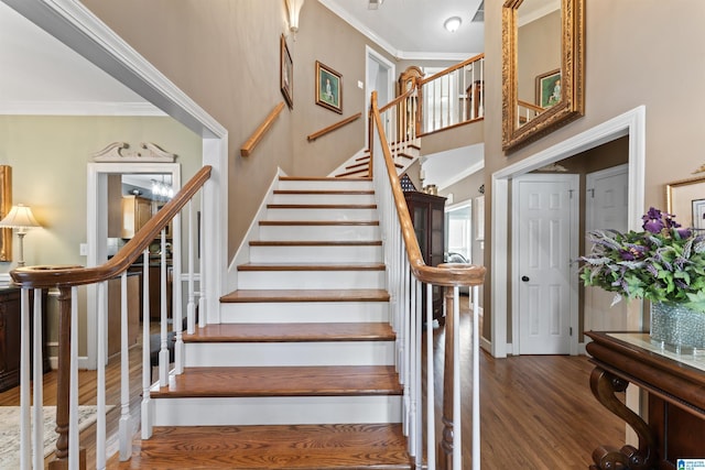 stairs featuring a high ceiling, baseboards, crown molding, and wood finished floors