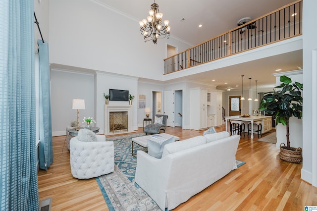 living room with crown molding, a fireplace, a notable chandelier, visible vents, and light wood-type flooring