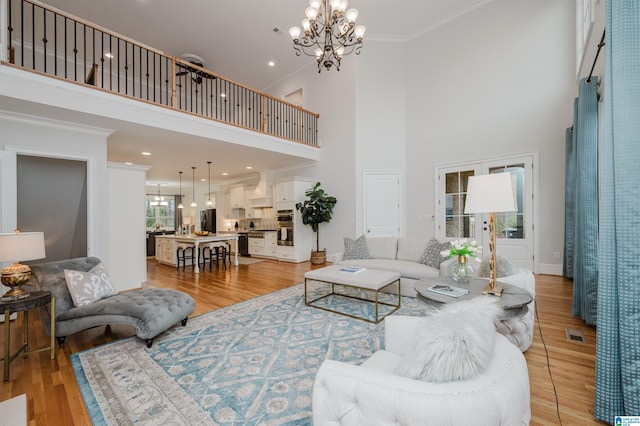 living area featuring light wood-type flooring, an inviting chandelier, a high ceiling, and ornamental molding