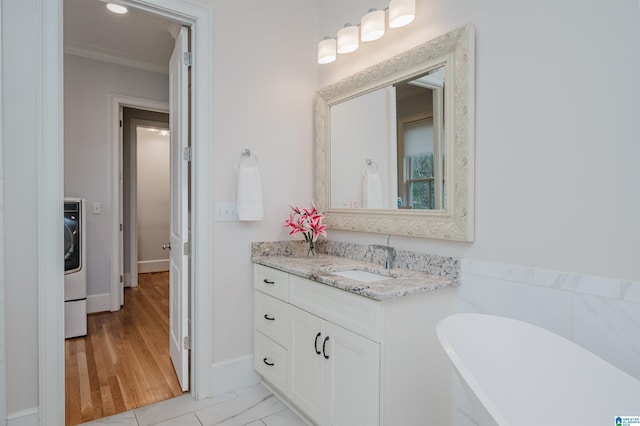 bathroom featuring vanity, marble finish floor, a soaking tub, washer / clothes dryer, and crown molding