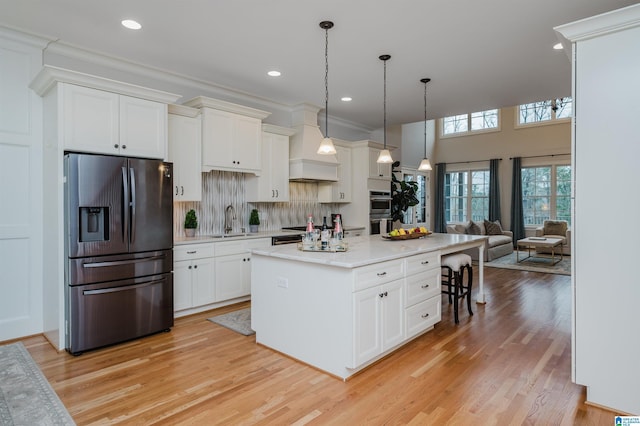 kitchen featuring decorative light fixtures, light countertops, appliances with stainless steel finishes, a kitchen island, and a sink