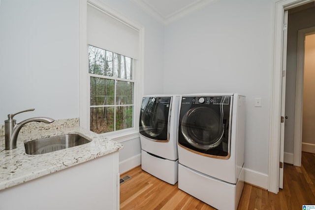 washroom featuring laundry area, a sink, light wood-type flooring, washing machine and clothes dryer, and crown molding