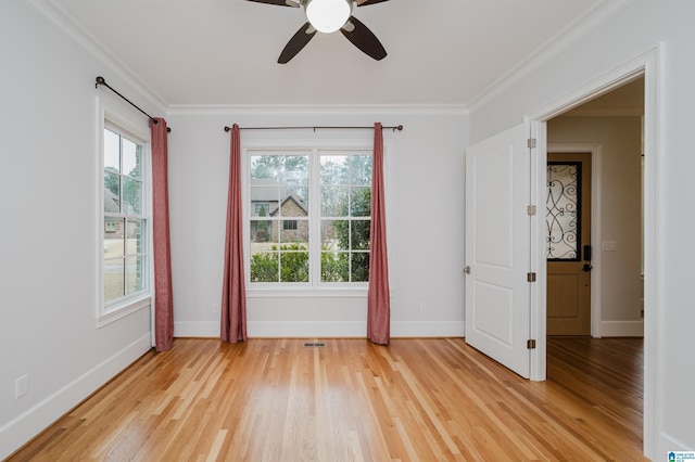 spare room featuring light wood-style floors, visible vents, crown molding, and baseboards