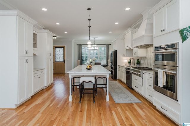 kitchen with white cabinets, custom range hood, light countertops, appliances with stainless steel finishes, and pendant lighting