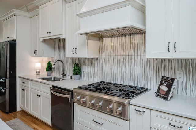 kitchen featuring custom exhaust hood, stainless steel appliances, light countertops, white cabinetry, and a sink