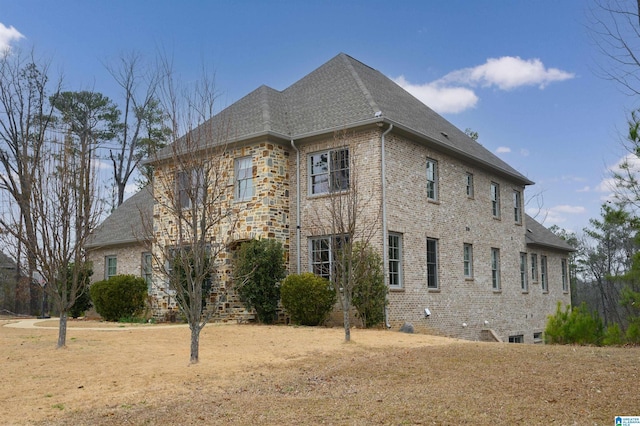 view of home's exterior with brick siding, a shingled roof, and a yard