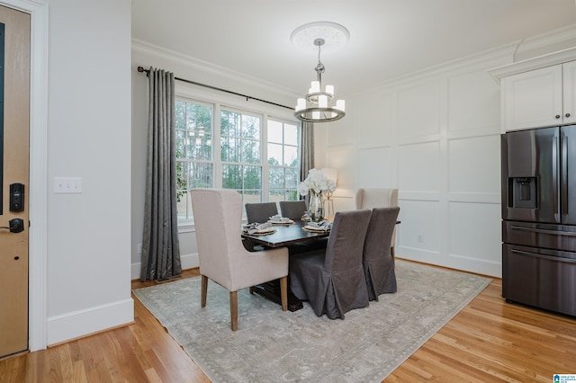 dining space with a decorative wall, light wood-style flooring, ornamental molding, a chandelier, and baseboards