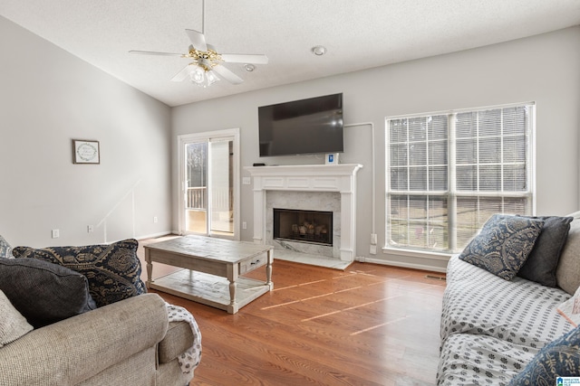 living room with a fireplace, ceiling fan, vaulted ceiling, a textured ceiling, and wood finished floors