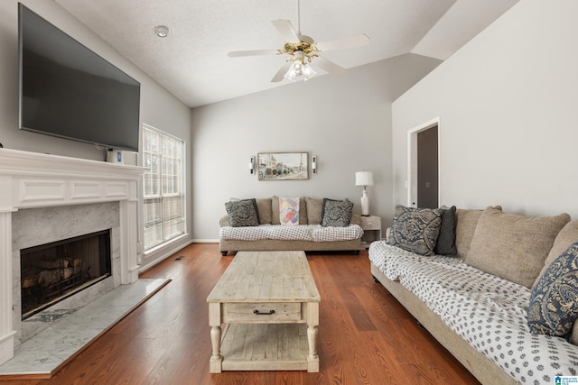 living area with a textured ceiling, dark wood-style flooring, a high end fireplace, a ceiling fan, and vaulted ceiling