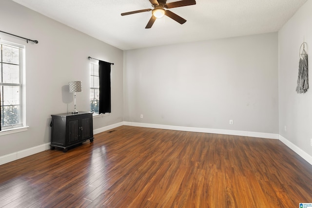 empty room with dark wood-type flooring, visible vents, baseboards, and a ceiling fan