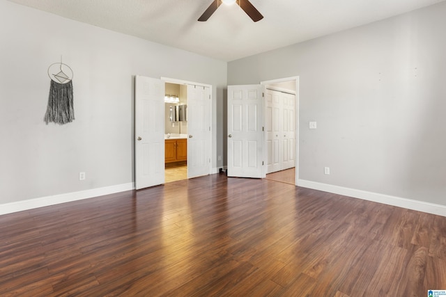 unfurnished bedroom with dark wood-type flooring, ensuite bath, baseboards, and a ceiling fan